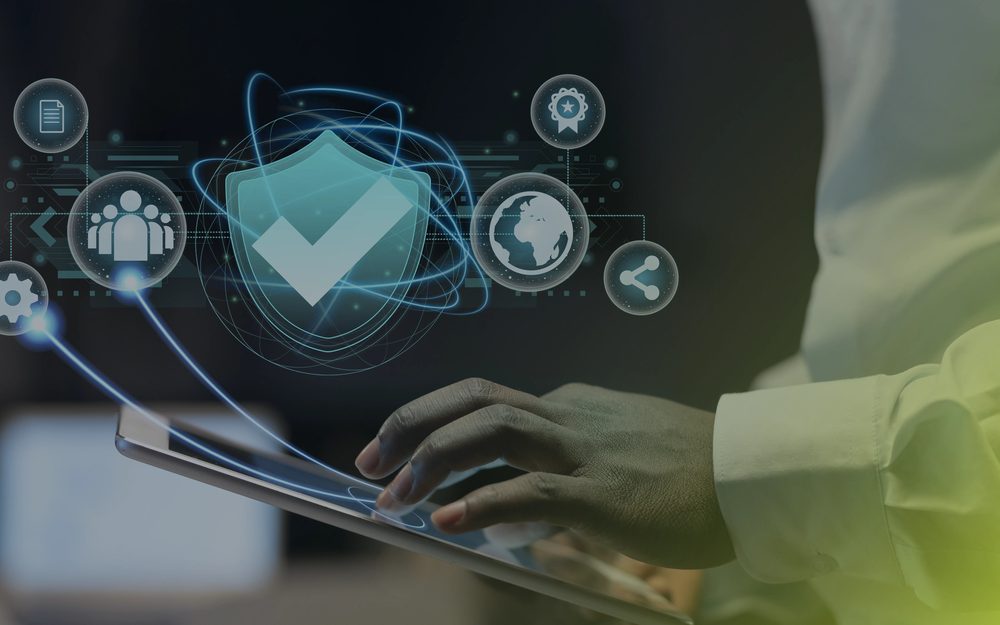 Hands using a tablet with a shield and check-mark security icon overlay