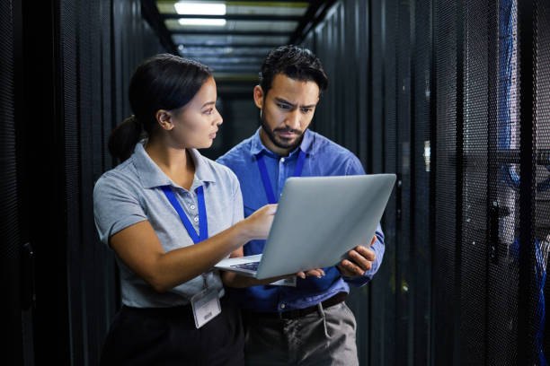 Two IT technicians reviewing a laptop in a server room